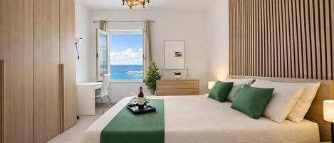 A modern bedroom with a large bed, a desk, and a view of the ocean.
