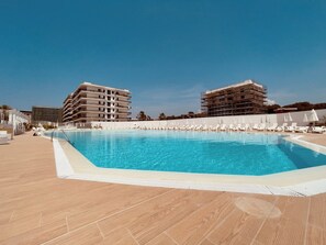 Une piscine avec des chaises longues et un bâtiment en arrière-plan.