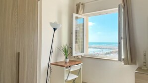 Une pièce avec un bureau, une plante en pot, une lampe et une fenêtre donnant sur la plage.