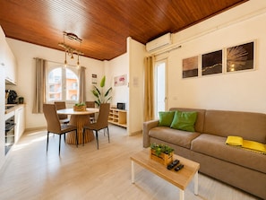 A modern living room with a wooden ceiling, a sofa, a coffee table, and a dining area with chairs and a table.