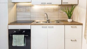 A modern kitchen with white cabinets, a stainless steel sink, and a black oven. - Demetra Sea Front Apartment (Castel Volturno)