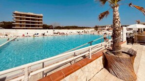 A swimming pool with a palm tree and a building in the background. - Demetra Sea Front Apartment (Castel Volturno)