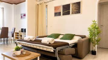A convertible sofa bed with a table and chairs in a room with a wooden ceiling, a wall-mounted air conditioner, and a potted plant.