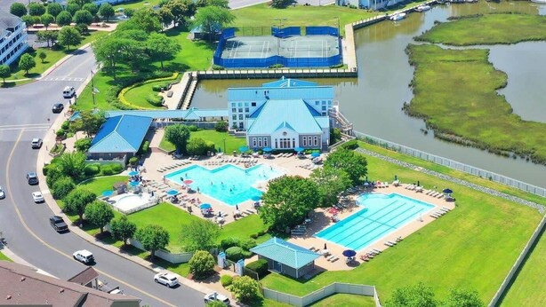 Vista aérea de un hotel con piscina, canchas de tenis y un lago.