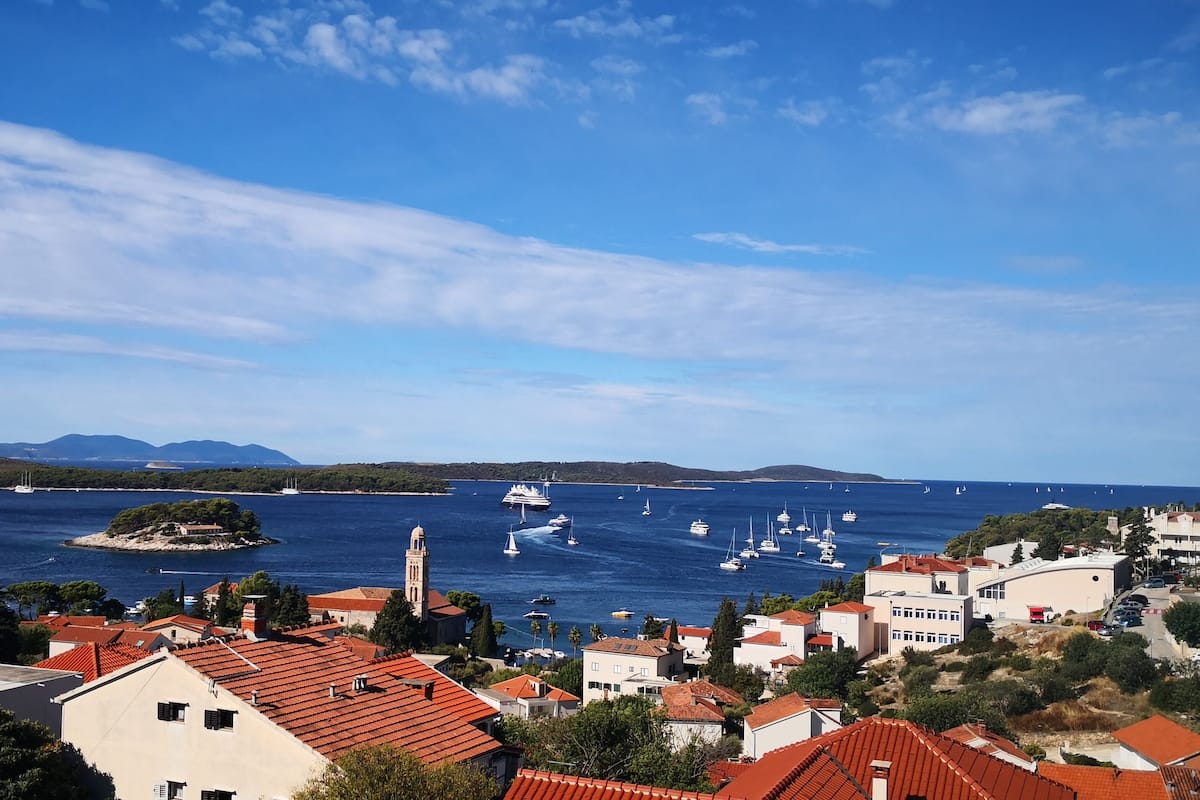 Un pueblo costero con edificios de tejados rojos, una iglesia destacada y un puerto deportivo con barcos.