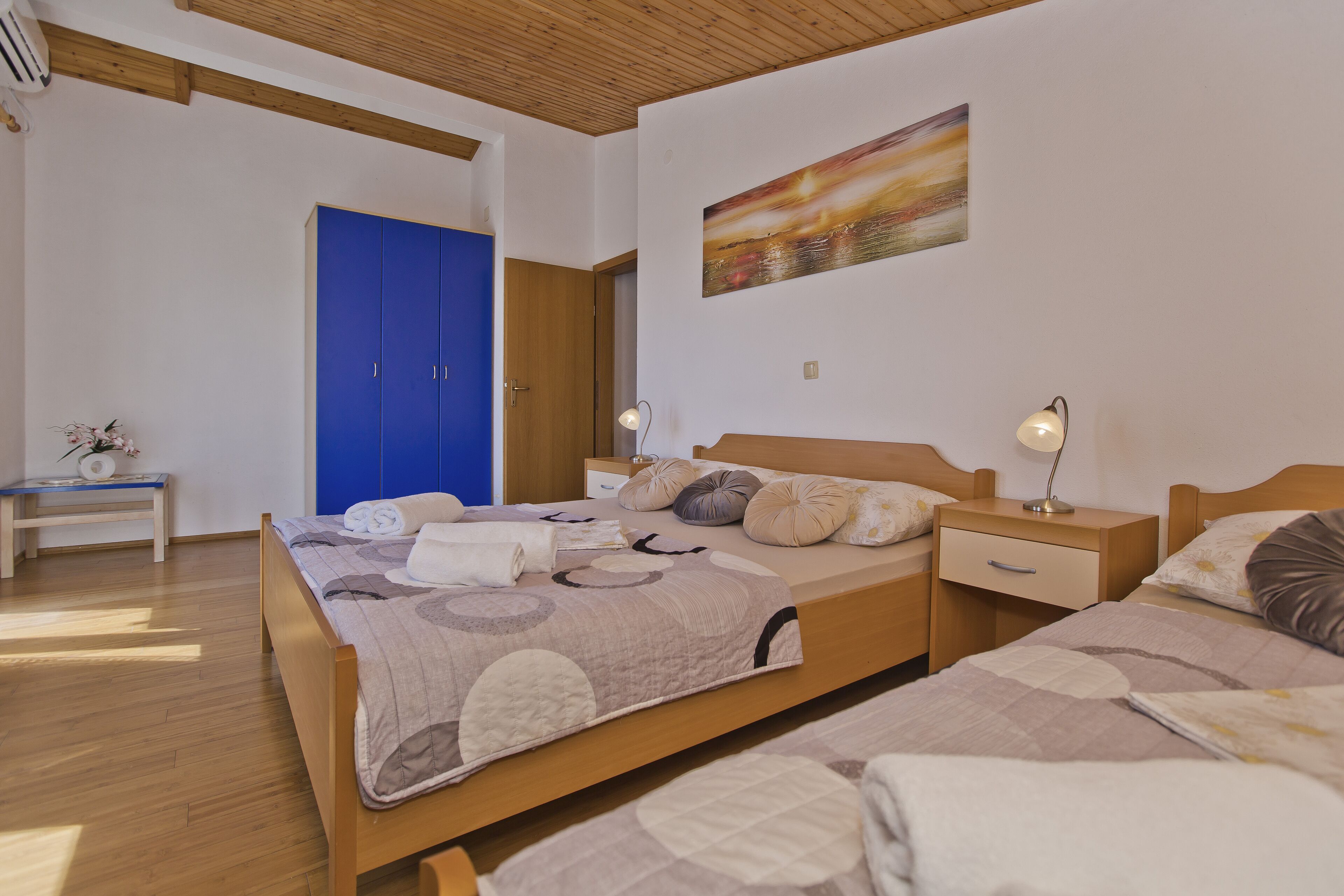 Un dormitorio con dos camas, una puerta azul, un cuadro y una mesita de noche con lámpara.