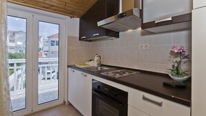 A modern kitchen with a dishwasher, oven, and a large window overlooking a balcony. - Apartmani Kresic 1 (Hvar)
