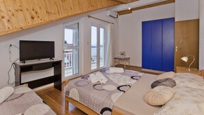 A bedroom with a bed, a desk with a TV, a blue wardrobe, and a balcony with a view. - Apartmani Kresic 1 (Hvar)