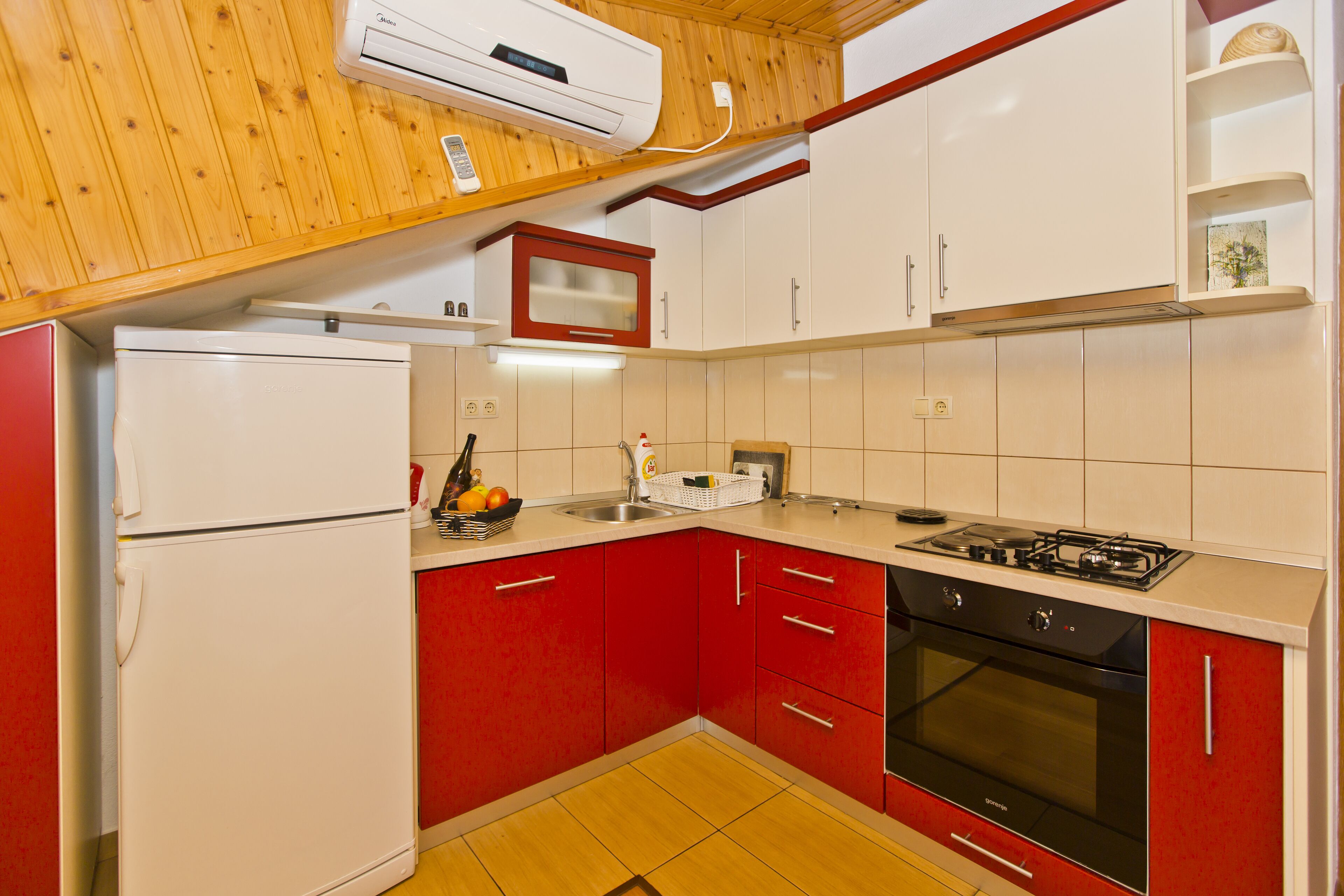 Cocina pequeña equipada con refrigerador, estufa, horno y armarios rojos.