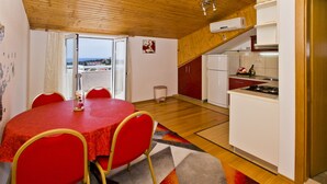 A compact kitchen with white cabinets, a red dining table, and a view through the open door. - Apartmani Kresic 1 (Hvar)
