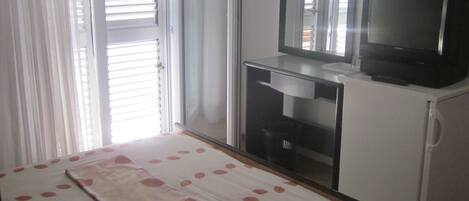 A bedroom with a bed, a television, a mirror, and a sliding door.