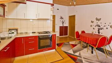 A compact kitchen with red and white cabinets, a built-in oven, and a dining area with a red table and chairs.