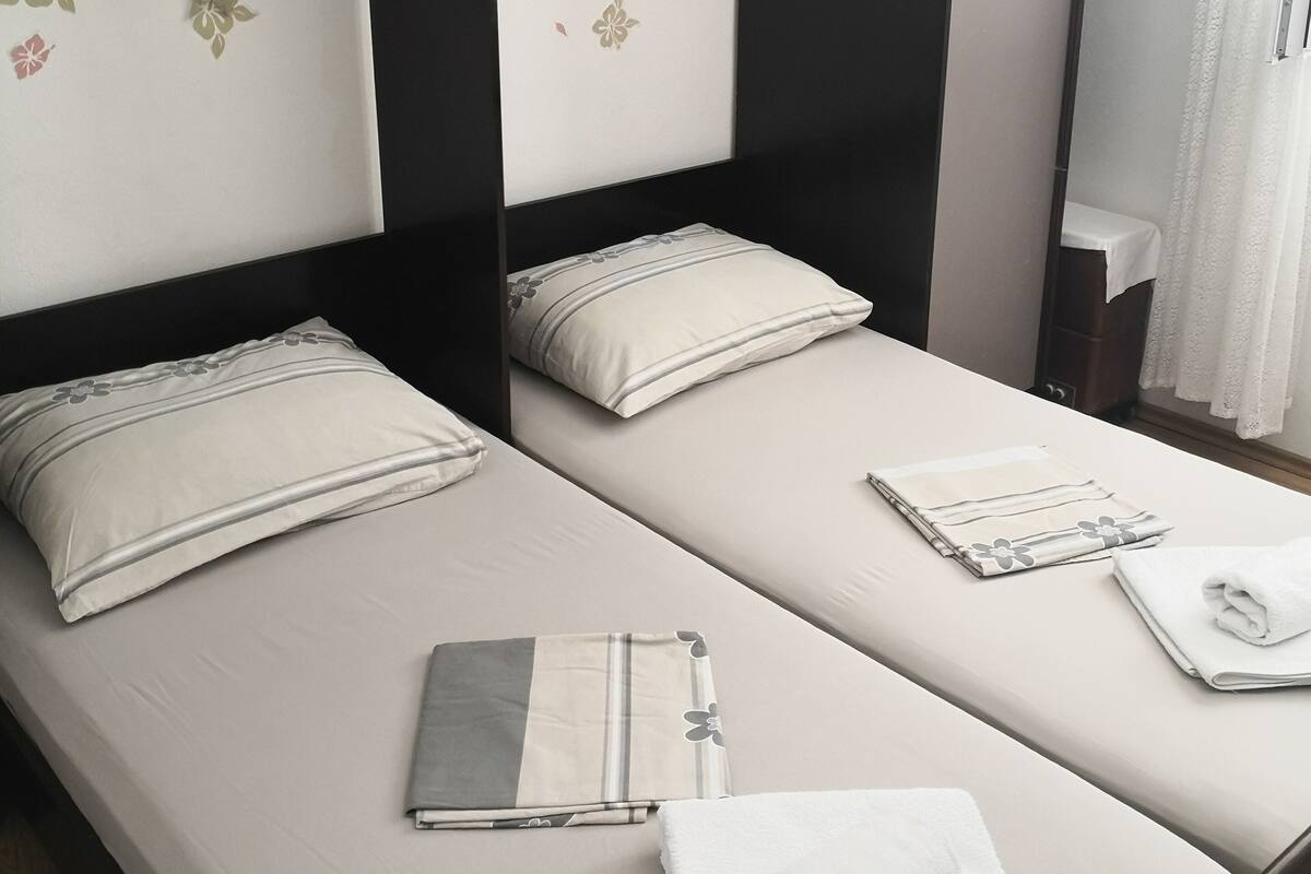 Habitación doble con dos camas, cada una con una almohada y una toalla doblada.