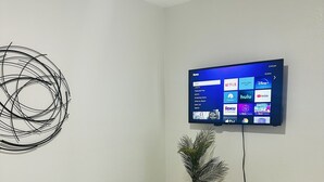 A bedroom with a bed, a wall-mounted TV displaying streaming services, a decorative wall piece, and a small plant on a nightstand. - Cozy and Modern apartment (Seffner)