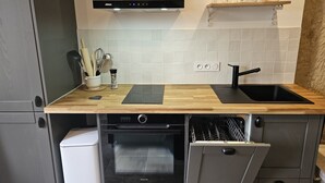 Una cucina compatta con forno a incasso, lavastoviglie, lavello nero e piano di lavoro in legno.