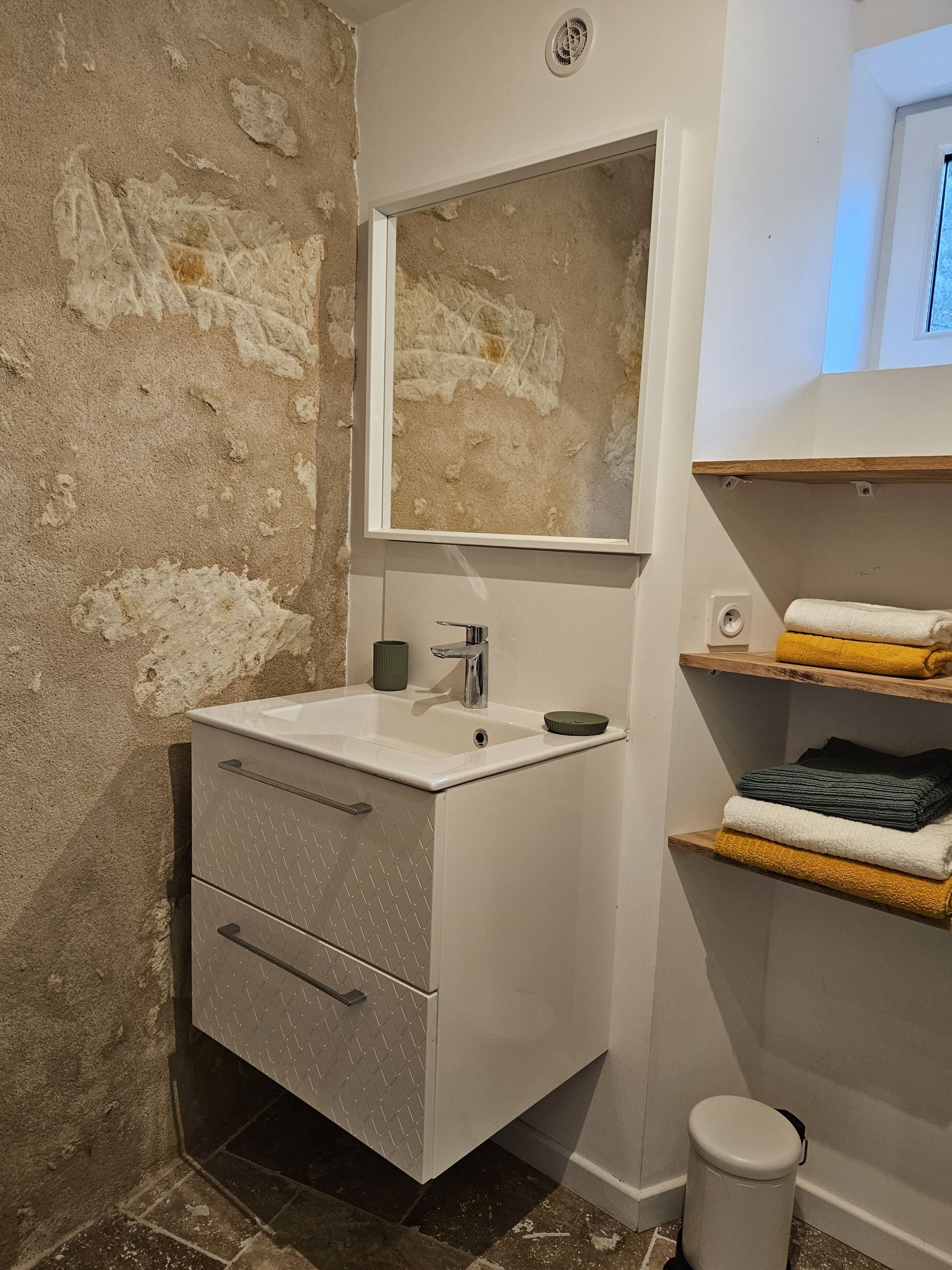 A bathroom with a white sink, a mirror, a toilet, and shelves with towels.