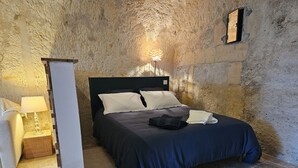 Una camera da letto con parete in pietra, un letto con biancheria scura, una lampada da comodino e un tavolino con lampada.