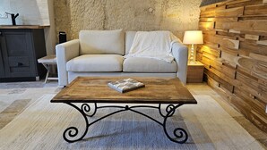 Un soggiorno con un divano color beige, un tavolino in legno, una lampada e una parete con texture.
