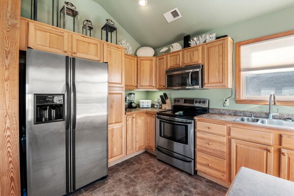 A kitchen with wooden cabinets, stainless steel appliances, and a window with blinds. - Sassy Seas: Pool | Hot Tub | Short Walk to Beach (Nags Head)