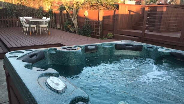 A hot tub with a control panel and jets, surrounded by a wooden deck and a fenced garden area. - Cozy Home in a Quiet Neighborhood

 (Vallejo)