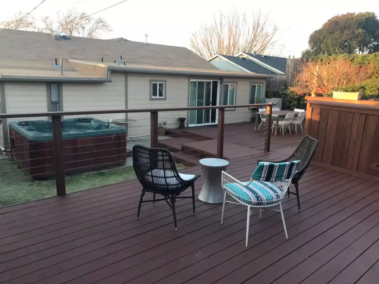 A wooden deck with two chairs and a table, a hot tub, and a covered patio area.