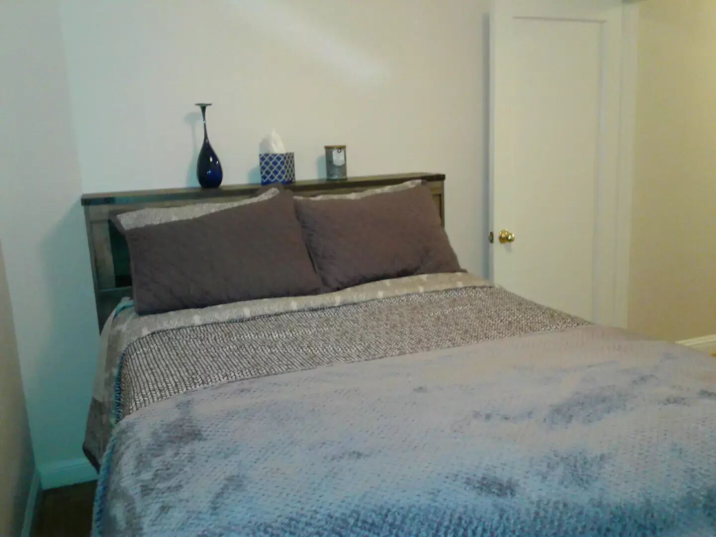A bed with a patterned bedspread, two pillows, and a bedside table with a vase and a tissue box.