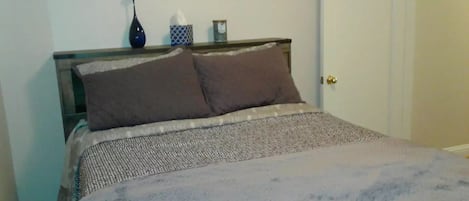 A bed with a patterned bedspread, two pillows, and a bedside table with a vase and a tissue box.