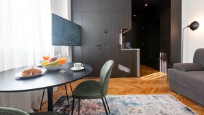 Una sala de estar moderna con una mesa de comedor, un sillón tapizado en verde, un televisor de pantalla plana y un sofá gris.