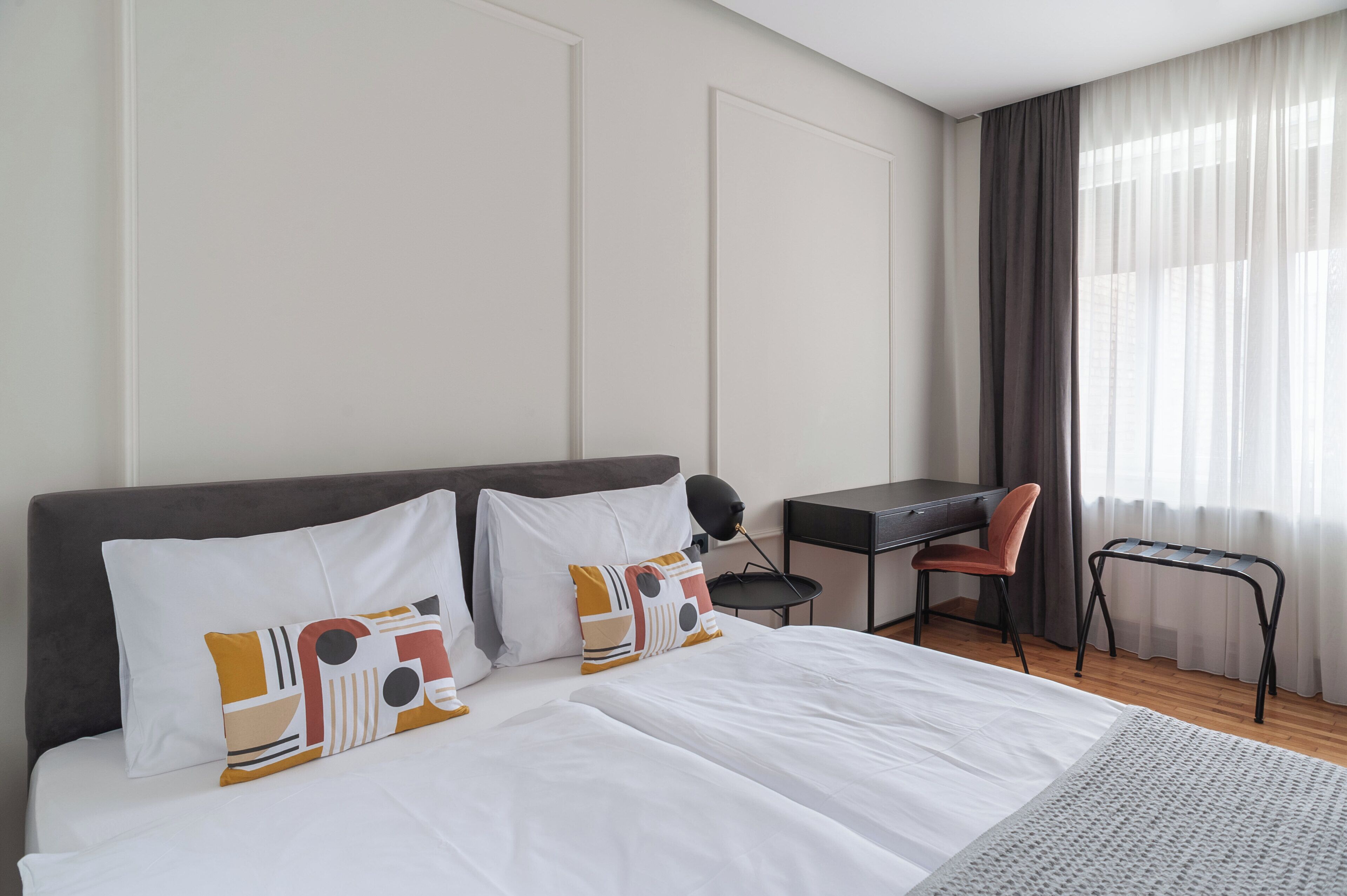 Habitación de hotel con cama, escritorio, silla y ventana con cortinas.