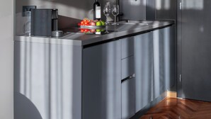 Una cocina moderna con gabinetes grises, encimera de acero inoxidable y suelo de madera.