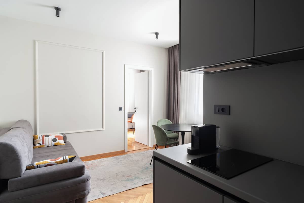 A compact living space with a kitchenette, a sofa with patterned cushions, a dining area with a table and chairs, and a door leading to another room.