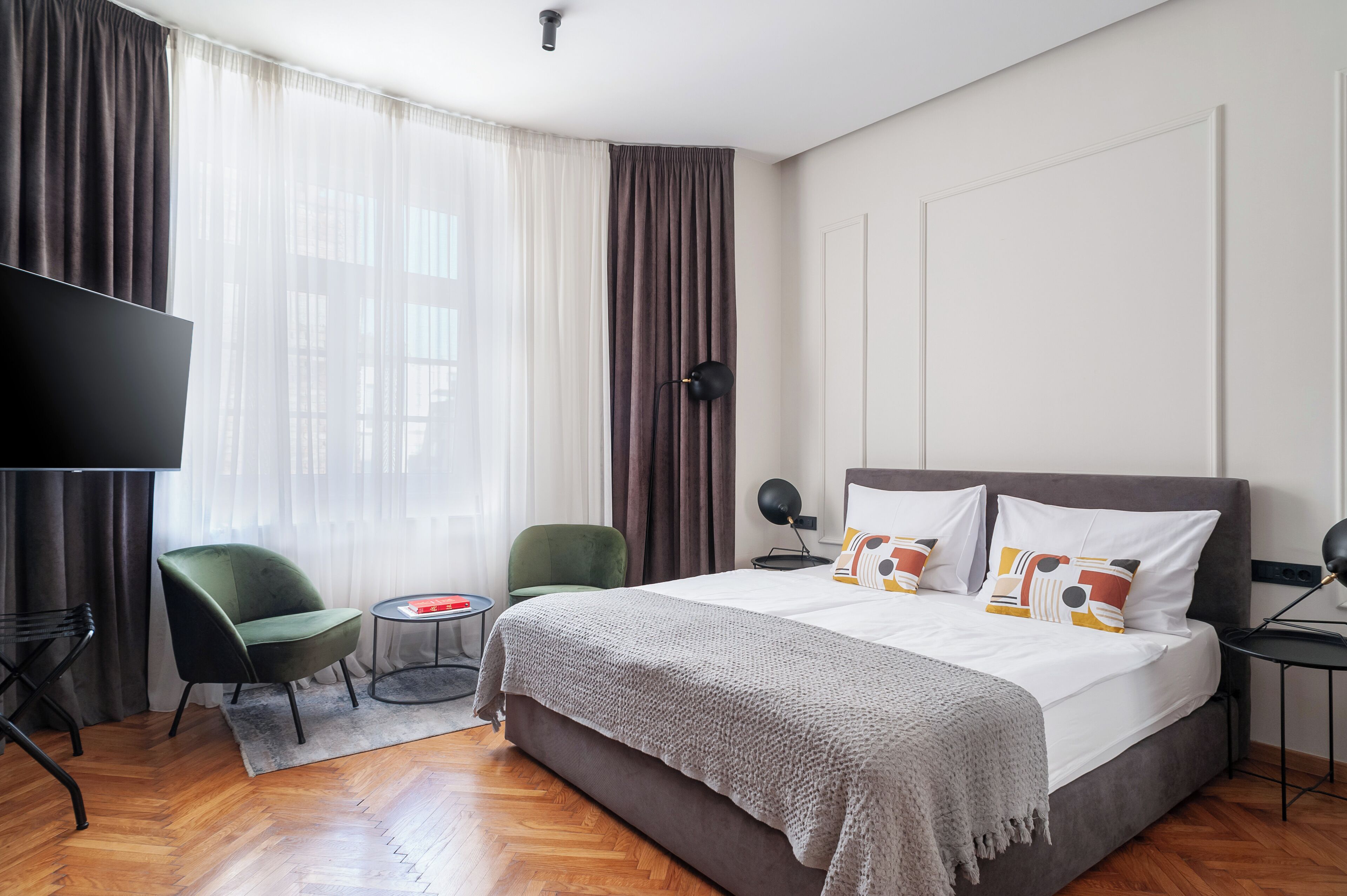 Une chambre d’hôtel moderne avec un grand lit, une télévision, un fauteuil vert et une petite table.