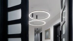 Un pasillo de diseño moderno, con una puerta negra con paneles de vidrio esmerilado, piso de mármol pulido y luces de techo circulares.