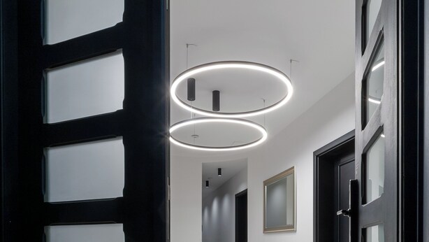 Un pasillo de diseño moderno, con una puerta negra con paneles de vidrio esmerilado, piso de mármol pulido y luces de techo circulares.