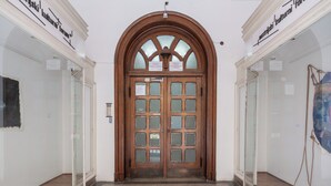Puerta doble de madera con paneles de vidrio, entre paredes blancas y un suelo de baldosas.