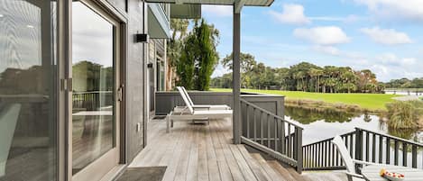 A wooden deck with a table and chairs, overlooking a body of water and a golf course.