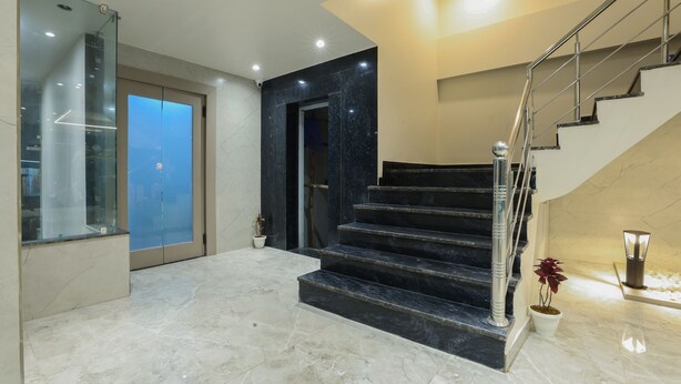 Een modern interieur met een marmeren trap, een glazen lift en een potplant.