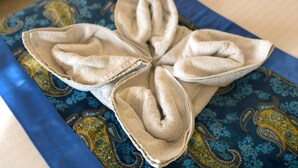 Een bed met een blauw en geel bedsprei met een paisleymotief en een wit, gestructureerd kussen in een bloemarrangement.