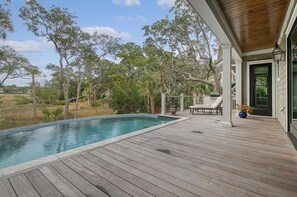 A wooden deck with a swimming pool, lounge chairs, and a view of the surrounding trees. - New Build, pool, marsh views (Kiawah Island)