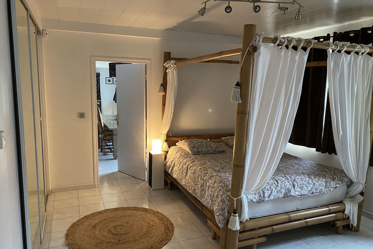 A bedroom with a four-poster bed, a bedside lamp, and a woven rug on the floor.