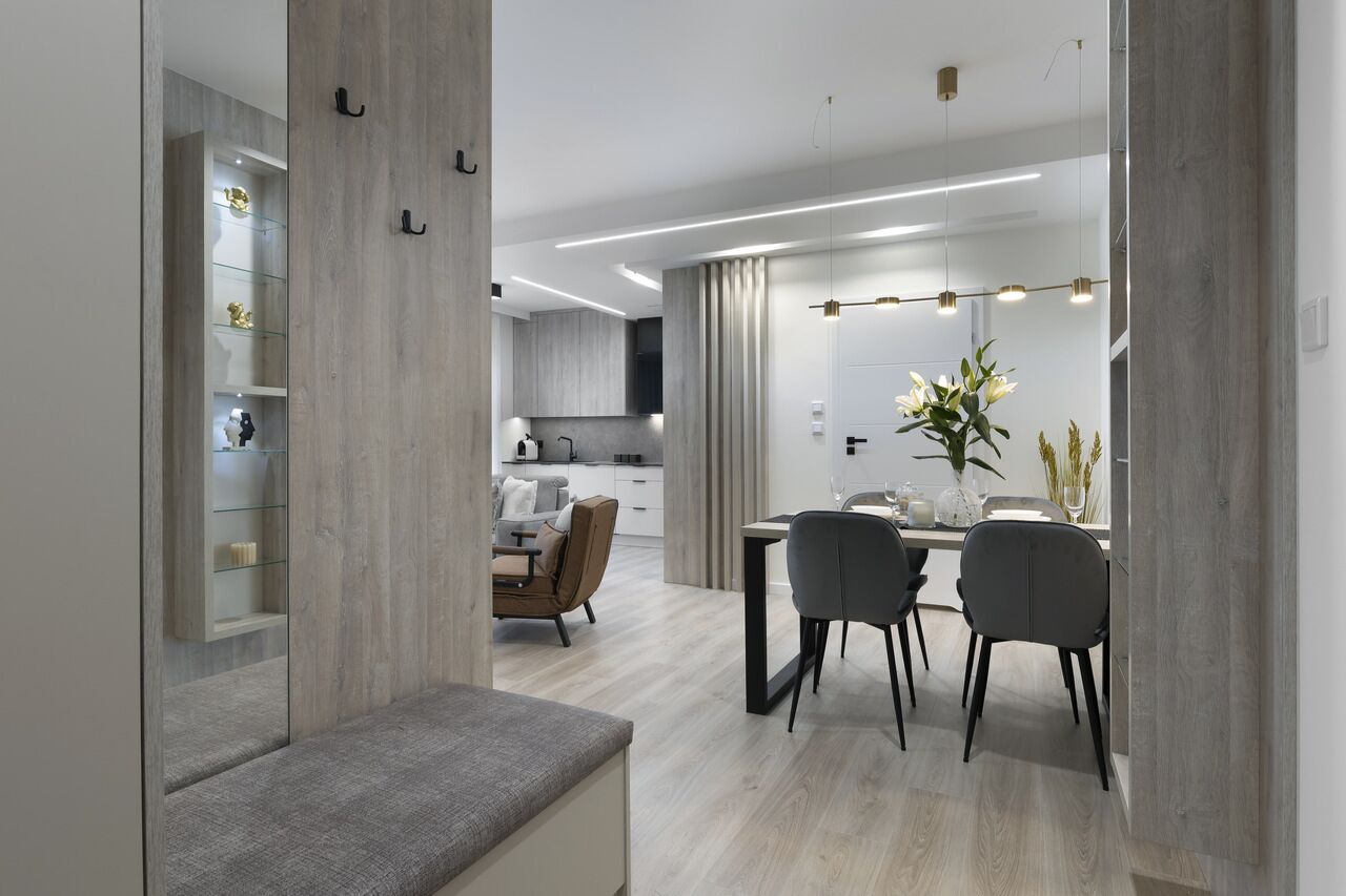 A modern dining area with a minimalist design, featuring a wooden bench, a dining table with four chairs, and a large mirror reflecting the space.