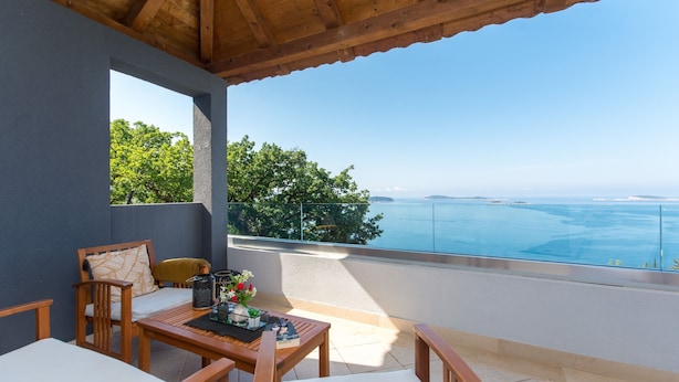 A balcony with a wooden table, chairs, and a view of the sea.