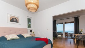 A bedroom with a large bed, a view of the sea, and a dining area with chairs and a table.