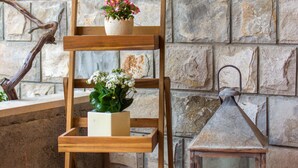 A wooden three-tiered shelf with potted plants against a stone wall.