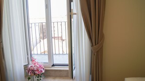 Une vue depuis une fenêtre, avec un arrangement floral sur le rebord, des rideaux à moitié tirés et un balcon en arrière-plan.