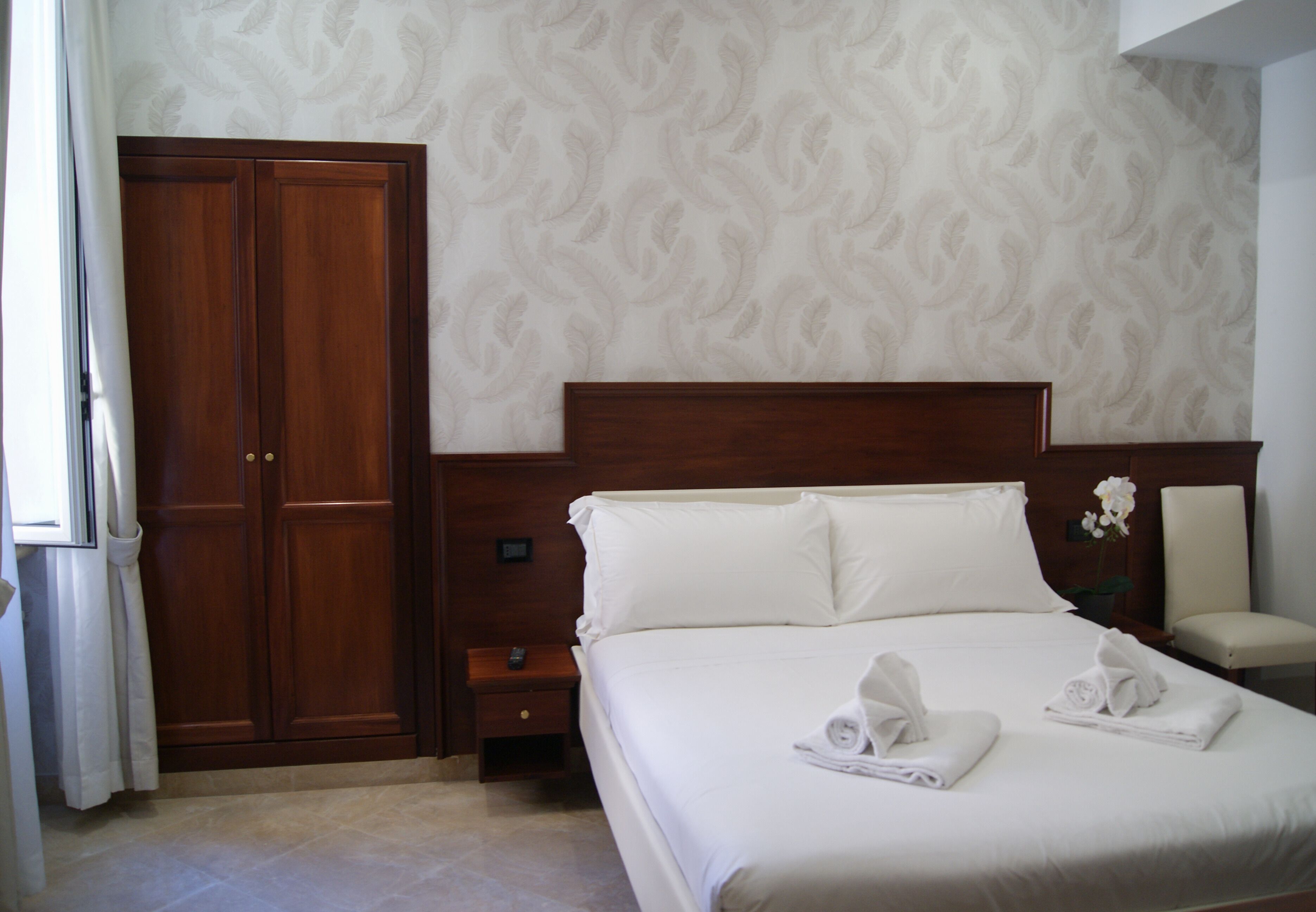 A hotel room with a large bed, wooden wardrobe, and a nightstand.