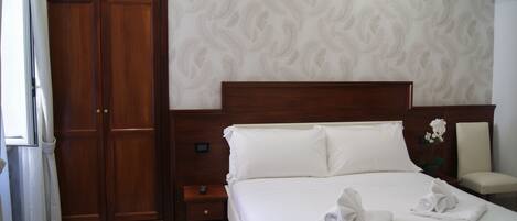 A hotel room with a large bed, wooden wardrobe, and a nightstand.