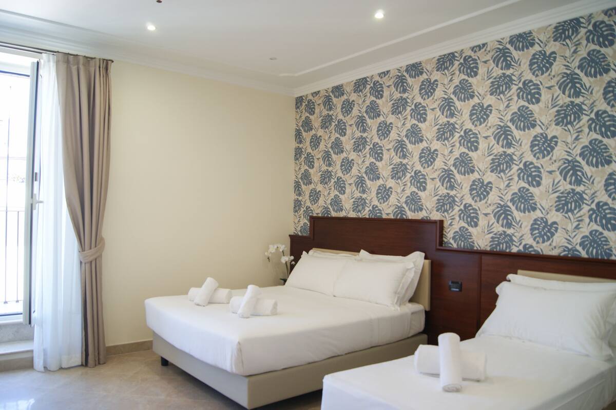 A hotel room with two beds, beige walls, and a floral wallpaper pattern.