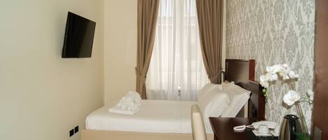 A hotel room with a bed, a desk with a telephone, a coffee maker, and a vase with flowers.