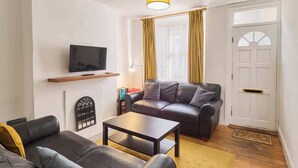 Ein Wohnzimmer mit einer Couch, einem Couchtisch, einem Fernseher auf einem Regal und einer Tür mit Fenster.